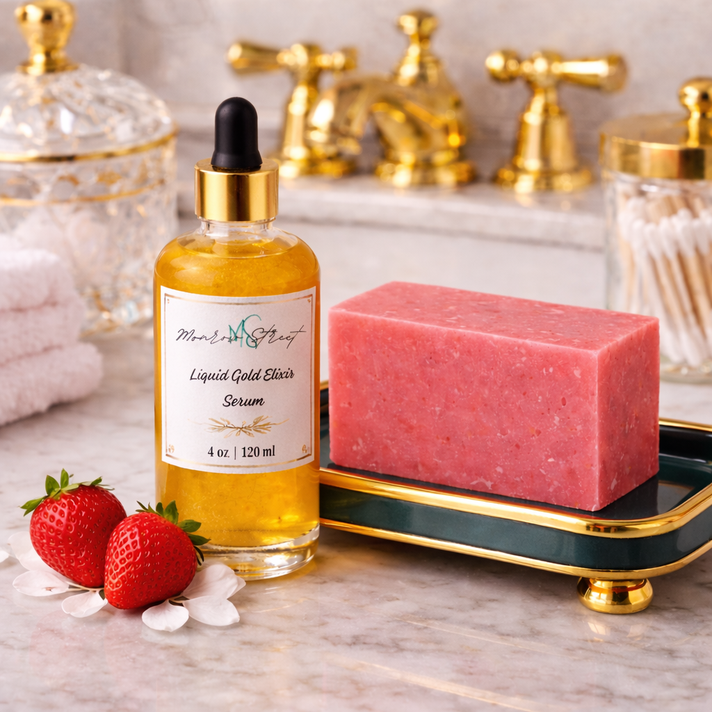 Glass dropper bottle labeled “Liquid Gold Elixir Serum” next to a pink handcrafted soap bar on a decorative tray, with fresh strawberries on a marble countertop and gold bathroom fixtures in the background.